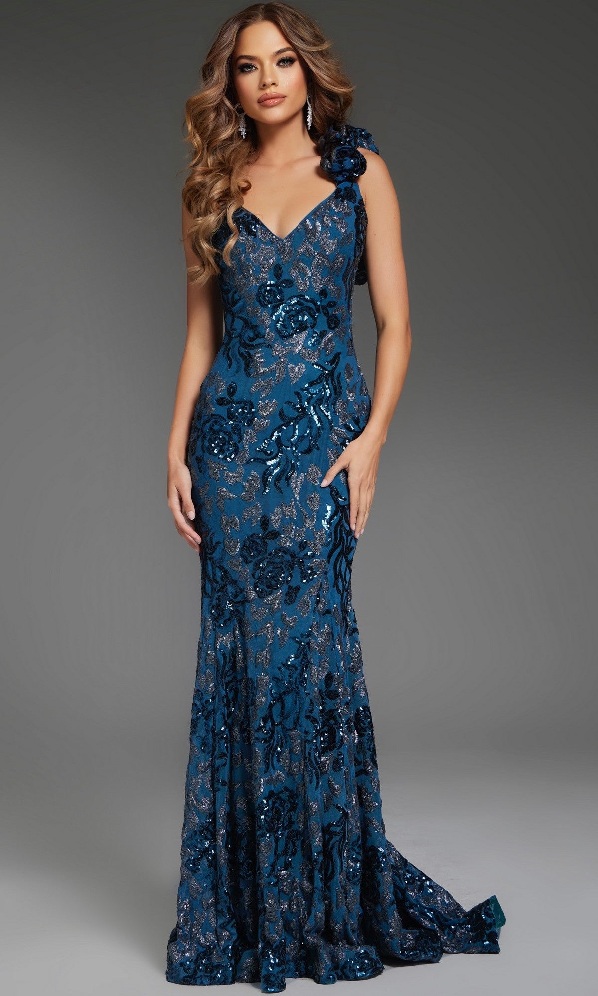 A woman poses against a plain gray background wearing the Jovani 37634 Long Prom Dress in slate—a fitted, floor-length mermaid gown with blue sequins, floral patterns, and a single shoulder strap.
